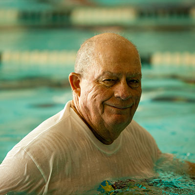 A man smiles as he walks laps in the pool.